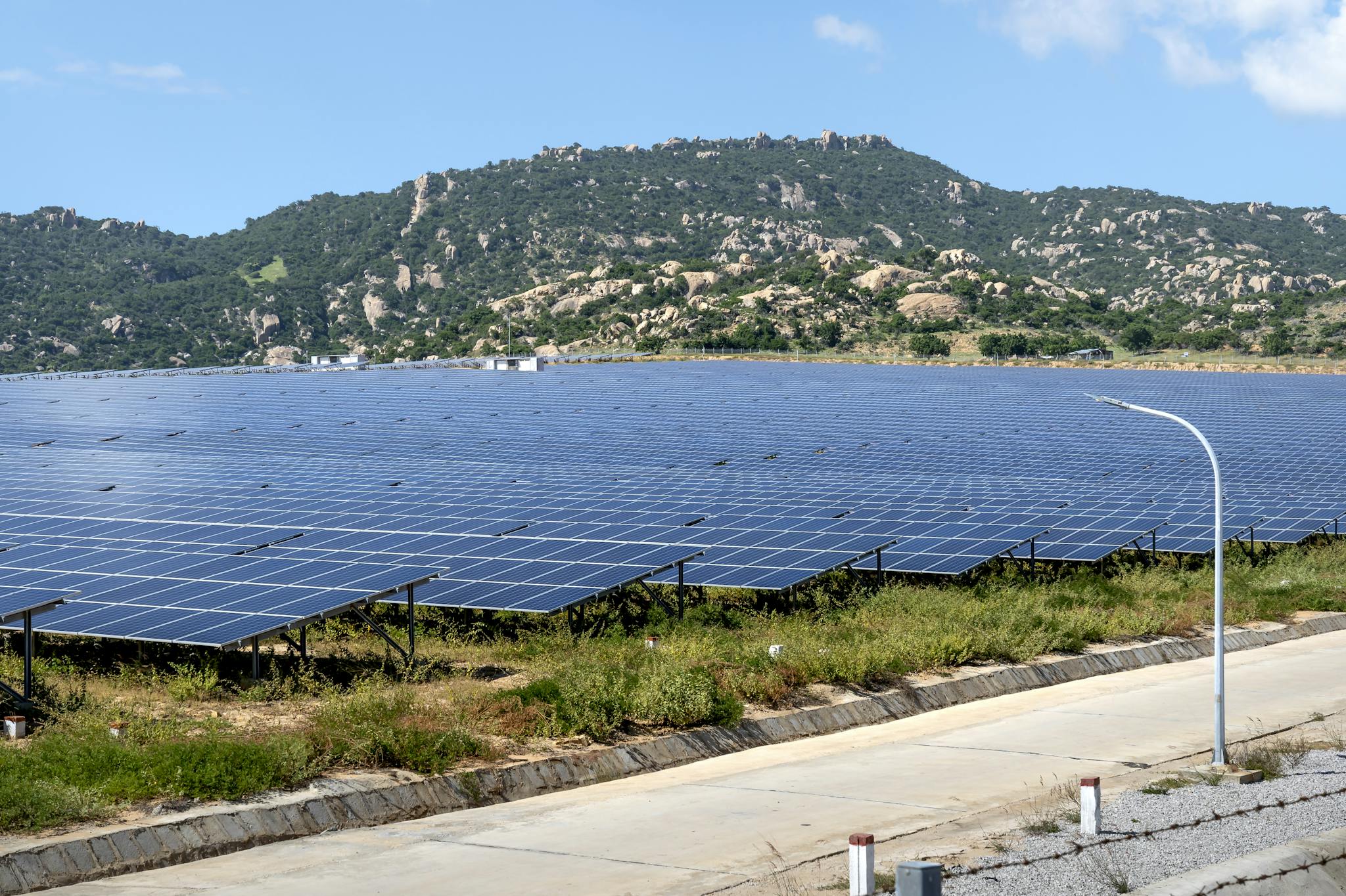 A vast solar farm set against a mountainous landscape under a blue sky.